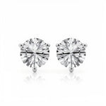 The image shows two stud earrings with large round-cut clear gemstones held by three-prong white metal settings. They are displayed side by side against a clean white background in a minimalist product photography style, unmounted on the ear. Bright, even lighting accentuates the facets of the stones and the polished finish of the metal while casting subtle reflections beneath each earring. The simple composition and stark backdrop bring full focus to the symmetrical arrangement and brilliance of the gems.