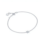 One delicate bracelet is shown, crafted from polished sterling silver with a slender cable chain and an adjustable spring-ring clasp accented by a tiny heart-shaped tag with brand name Adorn By You. A small starburst motif formed of marquise-cut clear crystals sits slightly off-center on the chain, each stone set in a minimal prong setting that catches the light. The piece is laid flat against a stark white background and illuminated by soft, diffuse studio lighting that creates an even, high-key aesthetic.