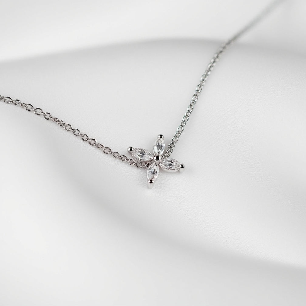 One delicate bracelet is shown, crafted from polished sterling silver with a slender cable chain and an adjustable spring-ring clasp accented by a tiny heart-shaped tag with brand name Adorn By You. A small starburst motif formed of marquise-cut clear crystals sits slightly off-center on the chain, each stone set in a minimal prong setting that catches the light. The piece is laid flat against a stark white background and illuminated by soft, diffuse studio lighting that creates an even, high-key aesthetic.
