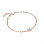 One rose gold chain bracelet is featured, crafted from delicate polished links with a four-petal flower motif at its center set with marquise-cut clear stones and a tiny signature heart tag with brand name Adorn By You by the spring-ring clasp. The warm metallic hue contrasts subtly with the sparkling white gems, arranged symmetrically in a simple botanical shape. The bracelet is displayed flat against a seamless white background under soft, even studio lighting that eliminates shadows | Adorn By You