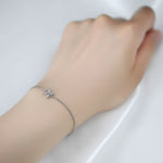 A single delicate silver chain bracelet features a tiny star-shaped charm set with clear marquise and round stones at its center. It\u2019s worn loosely on a slender wrist, with the hand resting gently on a smooth white silk surface. The lighting is soft and diffused, casting an even glow that enhances the polished metal and sparkling facets without harsh shadows. Shot in close-up with a shallow depth of field, the image has a minimalist, elegant product-photography style. | Adorn by You