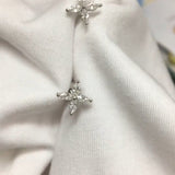 Two silver stud earrings with four clear, marquise-cut stones set in a prong-style cross are nestled into a crisp white fabric. The gemstones sparkle softly under diffused, natural light, their facets catching gentle highlights. Captured in a close-up with a shallow depth of field, the earrings are displayed pinned to the folds of the cloth against a softly blurred indoor background. | Adorn By You
